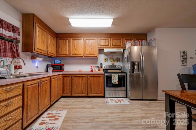 kitchen with brown cabinets, stainless steel appliances, light countertops, under cabinet range hood, and a sink