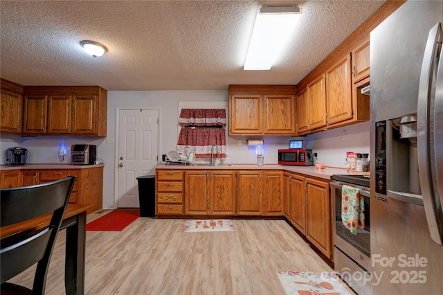 kitchen with brown cabinets, light wood finished floors, stainless steel appliances, and light countertops