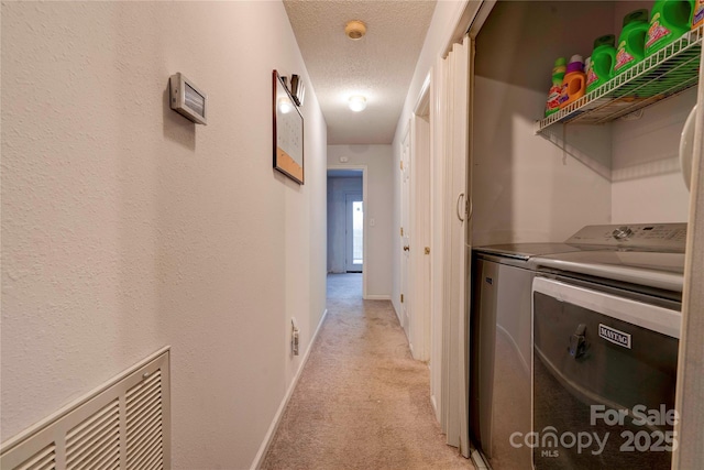 laundry area featuring light carpet, baseboards, visible vents, washing machine and clothes dryer, and a textured ceiling