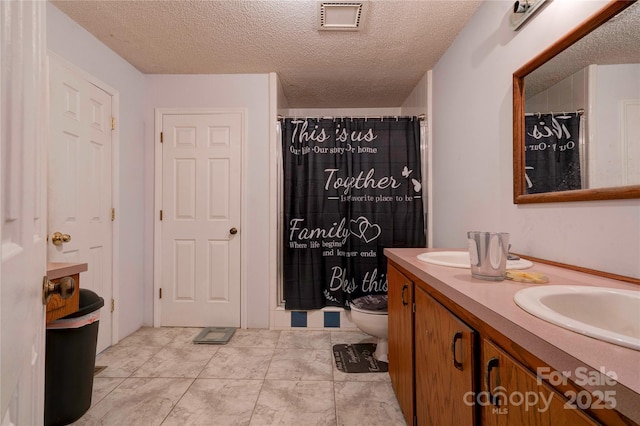 bathroom with double vanity, visible vents, and a textured ceiling