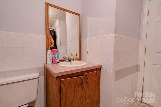 full bath featuring tile walls, toilet, wainscoting, vanity, and a textured ceiling