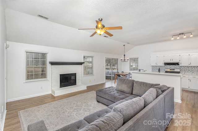 living room featuring a textured ceiling, light hardwood / wood-style floors, lofted ceiling, ceiling fan with notable chandelier, and a fireplace