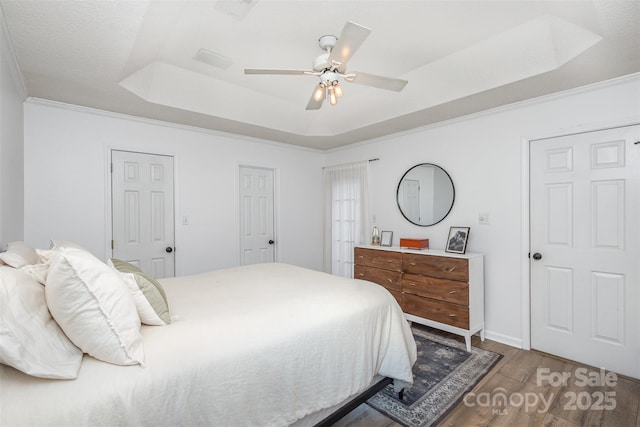 bedroom with hardwood / wood-style flooring, ceiling fan, a tray ceiling, and crown molding