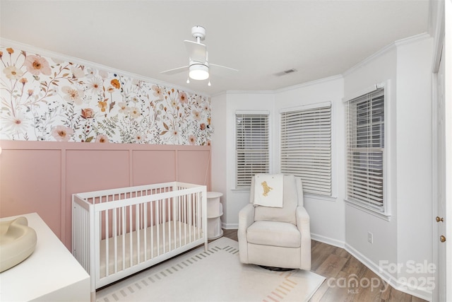 bedroom featuring hardwood / wood-style floors, a nursery area, ceiling fan, and ornamental molding