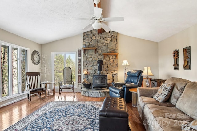 living room with lofted ceiling, ceiling fan, hardwood / wood-style flooring, a textured ceiling, and a wood stove