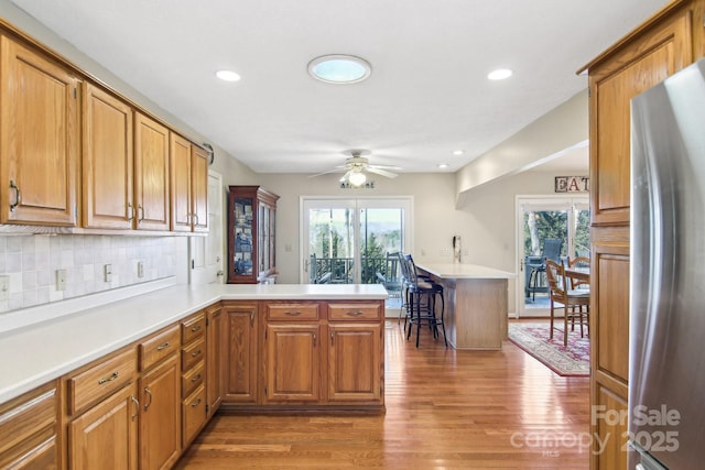 kitchen with wood-type flooring, backsplash, stainless steel fridge, kitchen peninsula, and ceiling fan