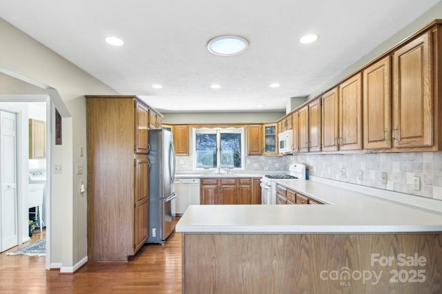 kitchen with tasteful backsplash, kitchen peninsula, white appliances, and light hardwood / wood-style flooring