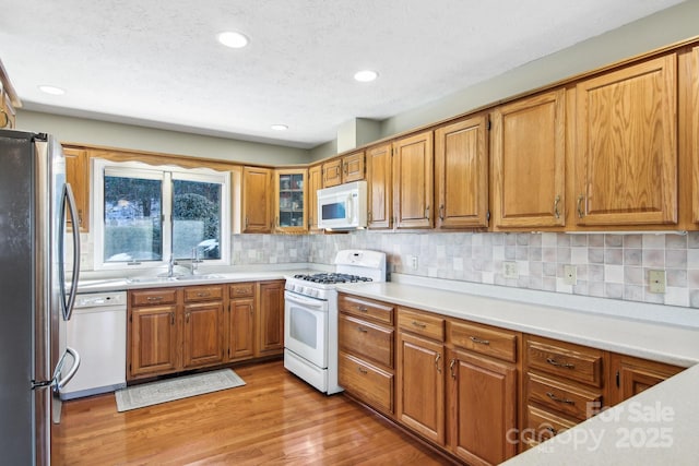 kitchen featuring sink, decorative backsplash, light hardwood / wood-style flooring, and white appliances