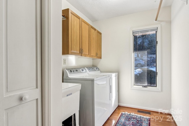 clothes washing area with light hardwood / wood-style floors, a textured ceiling, washing machine and dryer, cabinets, and sink