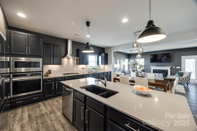 kitchen featuring stainless steel appliances, sink, tasteful backsplash, wall chimney range hood, and pendant lighting