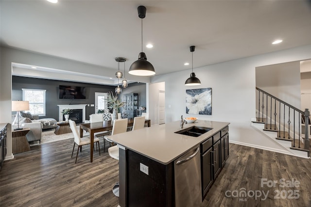 kitchen with a kitchen island with sink, hanging light fixtures, dark wood-type flooring, sink, and stainless steel dishwasher