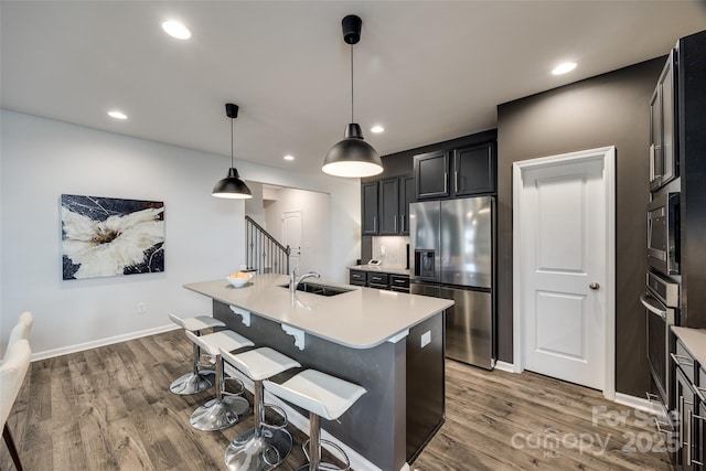 kitchen with a center island with sink, appliances with stainless steel finishes, a kitchen bar, sink, and decorative light fixtures