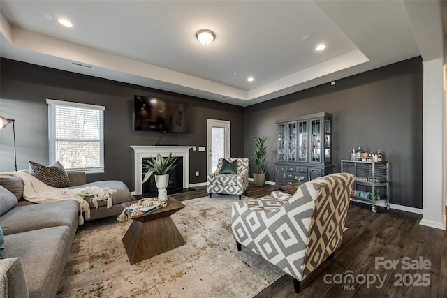 living room featuring dark hardwood / wood-style flooring, a high end fireplace, and a tray ceiling