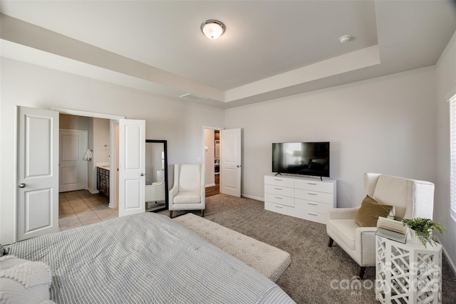 carpeted bedroom with ensuite bath and a tray ceiling