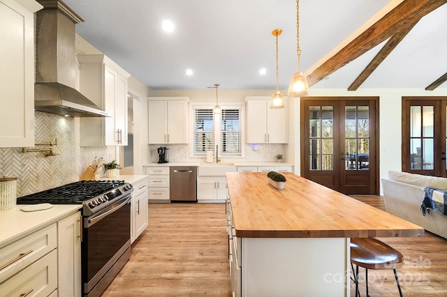 kitchen with french doors, stainless steel gas range, a kitchen island, wall chimney range hood, and white cabinetry