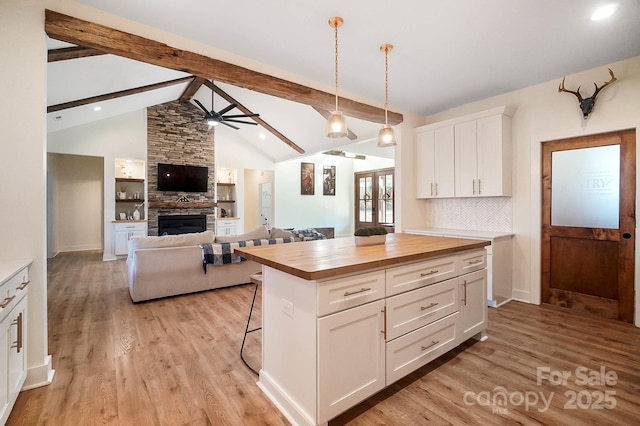 kitchen with wood counters, a kitchen bar, a kitchen island, vaulted ceiling with beams, and white cabinetry