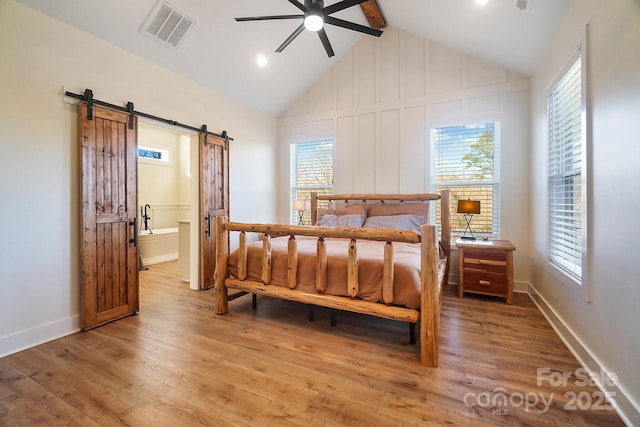 bedroom featuring a barn door, ceiling fan, light hardwood / wood-style floors, and vaulted ceiling with beams