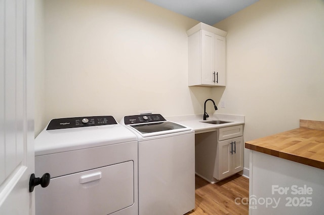 laundry area with washing machine and clothes dryer, light hardwood / wood-style floors, cabinets, and sink