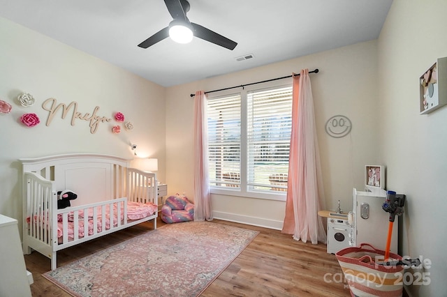 bedroom featuring ceiling fan, wood-type flooring, and a crib