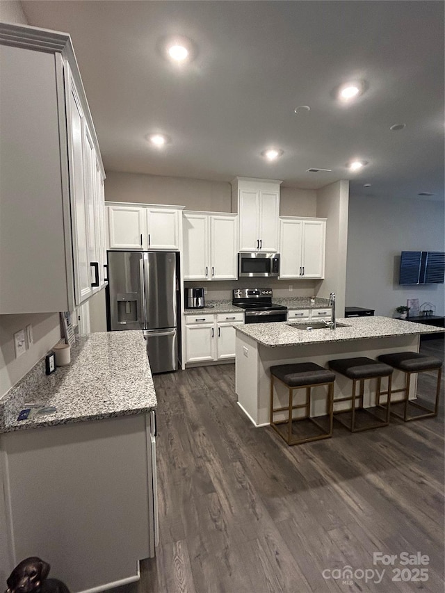 kitchen with dark wood-type flooring, appliances with stainless steel finishes, white cabinets, and an island with sink