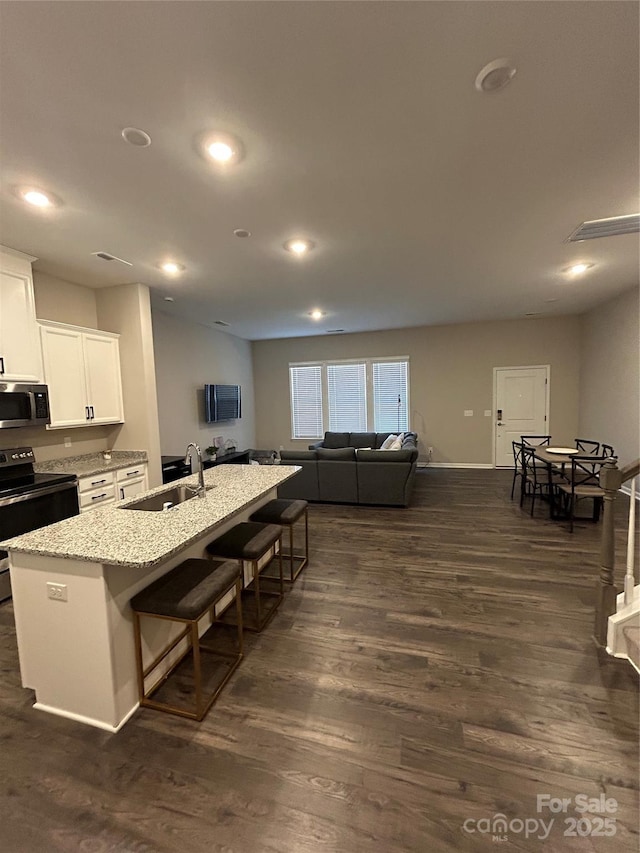 kitchen with a breakfast bar, black range with electric stovetop, sink, an island with sink, and white cabinets