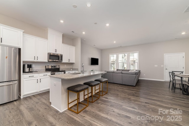 kitchen with appliances with stainless steel finishes, a kitchen island with sink, white cabinets, and light stone counters