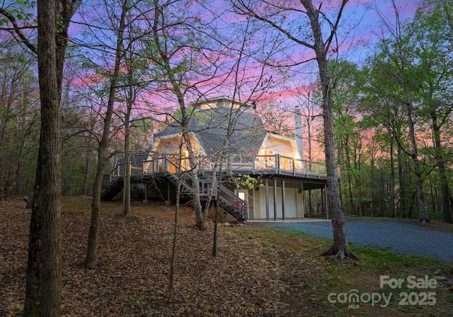 rear view of house featuring gravel driveway, stairway, a wooden deck, and an attached garage
