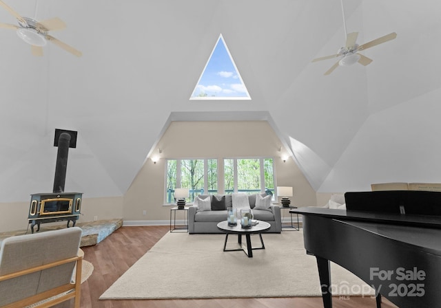 living room featuring baseboards, a ceiling fan, a wood stove, lofted ceiling, and wood finished floors
