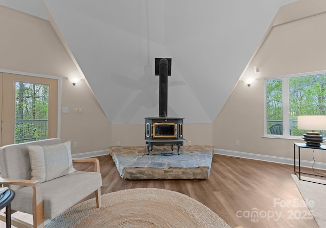 living area with a wood stove, lofted ceiling, baseboards, and wood finished floors