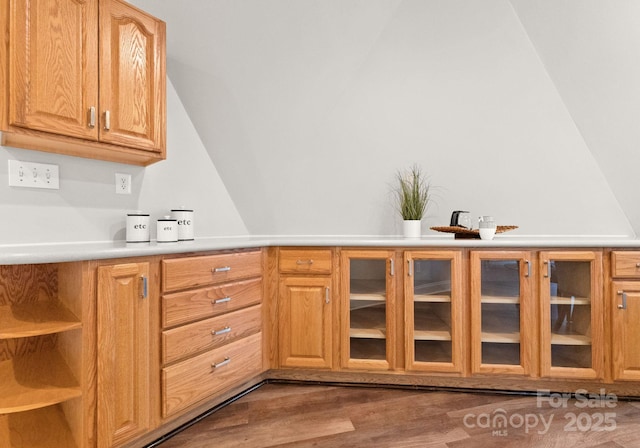 kitchen with lofted ceiling, glass insert cabinets, light countertops, and wood finished floors