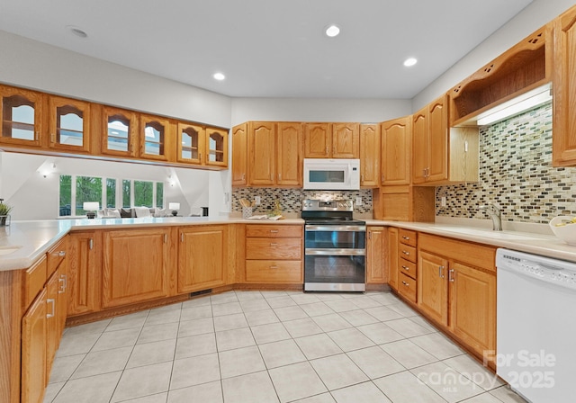 kitchen with white appliances, glass insert cabinets, light countertops, decorative backsplash, and a sink