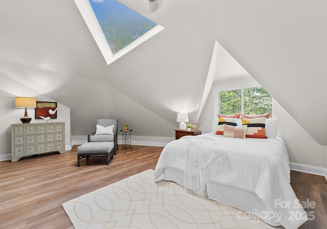 bedroom featuring vaulted ceiling with skylight, wood finished floors, and baseboards