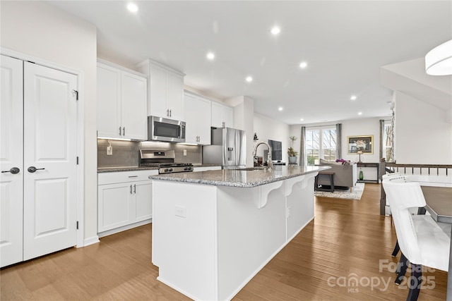 kitchen with dark stone countertops, stainless steel appliances, white cabinets, and a center island with sink