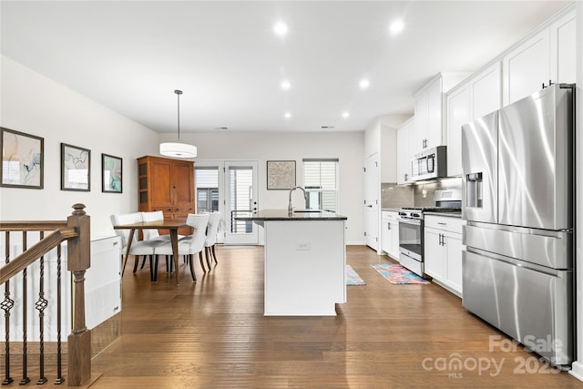 kitchen with white cabinetry, tasteful backsplash, decorative light fixtures, appliances with stainless steel finishes, and a kitchen island with sink