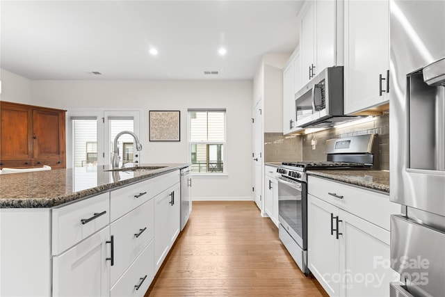 kitchen featuring sink, stainless steel appliances, white cabinets, a center island with sink, and dark stone counters