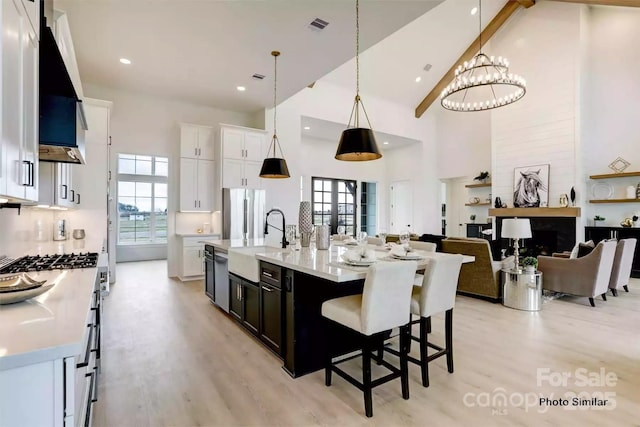 kitchen featuring decorative light fixtures, a center island with sink, beam ceiling, white cabinetry, and high vaulted ceiling