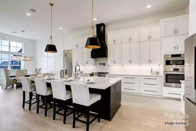 kitchen with white cabinetry, an island with sink, stainless steel double oven, and custom exhaust hood