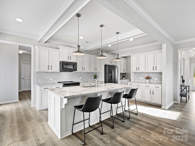 kitchen with hanging light fixtures, range with electric stovetop, stainless steel fridge, an island with sink, and white cabinets