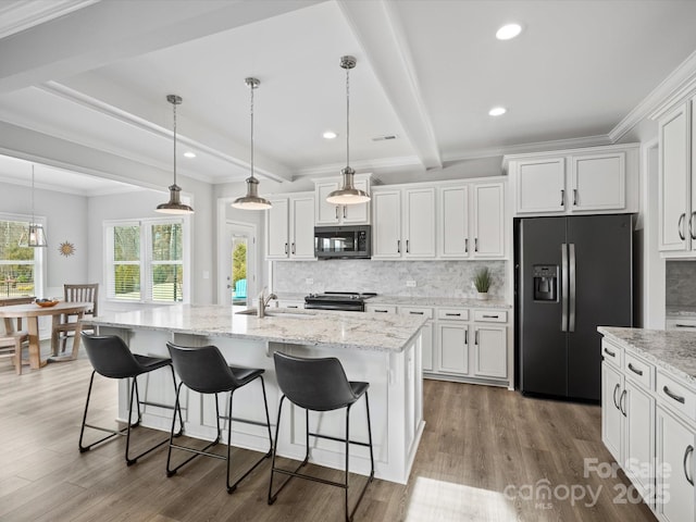 kitchen with appliances with stainless steel finishes, white cabinetry, a kitchen island with sink, beam ceiling, and tasteful backsplash