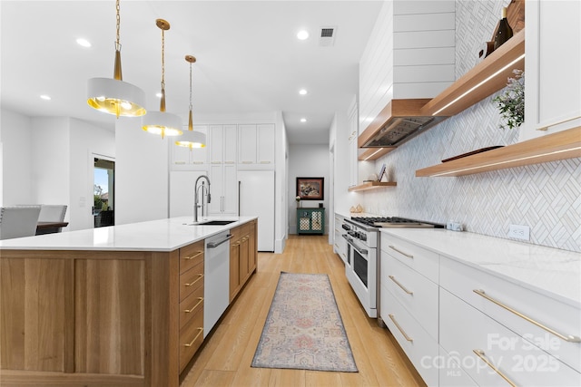 kitchen featuring white cabinetry, a center island with sink, appliances with stainless steel finishes, decorative light fixtures, and sink