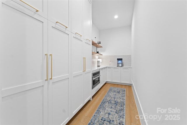 kitchen with tasteful backsplash, light hardwood / wood-style flooring, oven, and white cabinetry