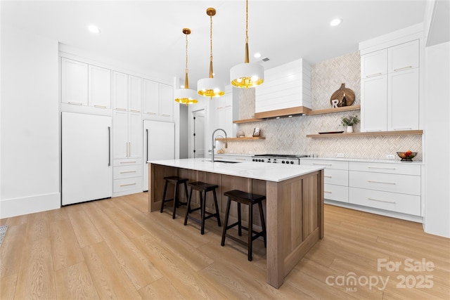 kitchen featuring premium range hood, white cabinetry, backsplash, paneled built in refrigerator, and sink