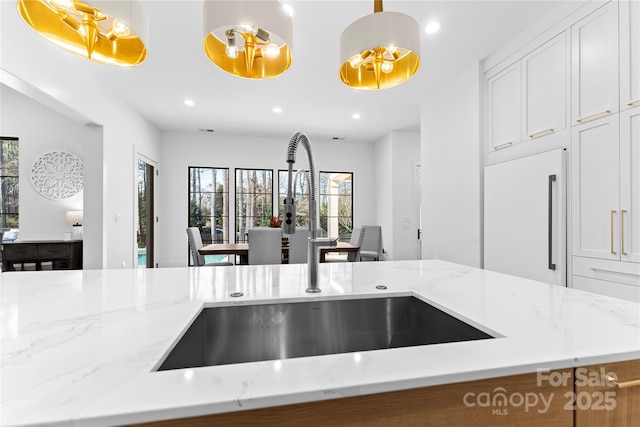 kitchen featuring decorative light fixtures, sink, white built in fridge, white cabinetry, and light stone counters