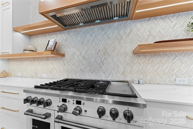 kitchen with double oven range, backsplash, wall chimney exhaust hood, white cabinets, and light stone counters