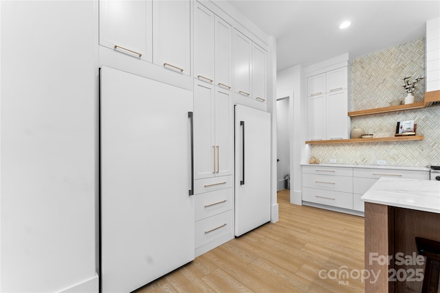 kitchen featuring backsplash, paneled built in refrigerator, white cabinetry, and light hardwood / wood-style flooring