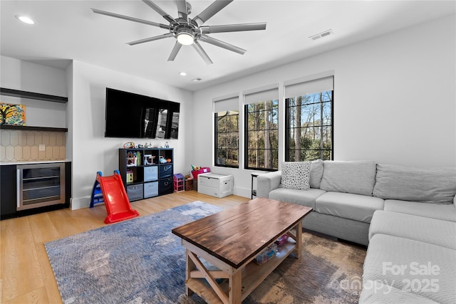 living room featuring hardwood / wood-style flooring, bar area, beverage cooler, and ceiling fan