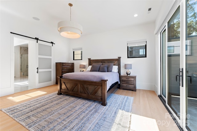 bedroom with light hardwood / wood-style floors, ensuite bathroom, and a barn door