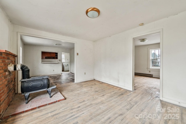 sitting room featuring light hardwood / wood-style floors, a wood stove, and a baseboard heating unit