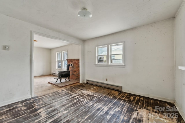 spare room featuring hardwood / wood-style flooring, a wood stove, and a baseboard radiator