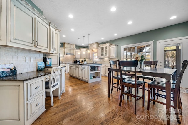 kitchen with a center island, cream cabinets, light hardwood / wood-style floors, backsplash, and hanging light fixtures